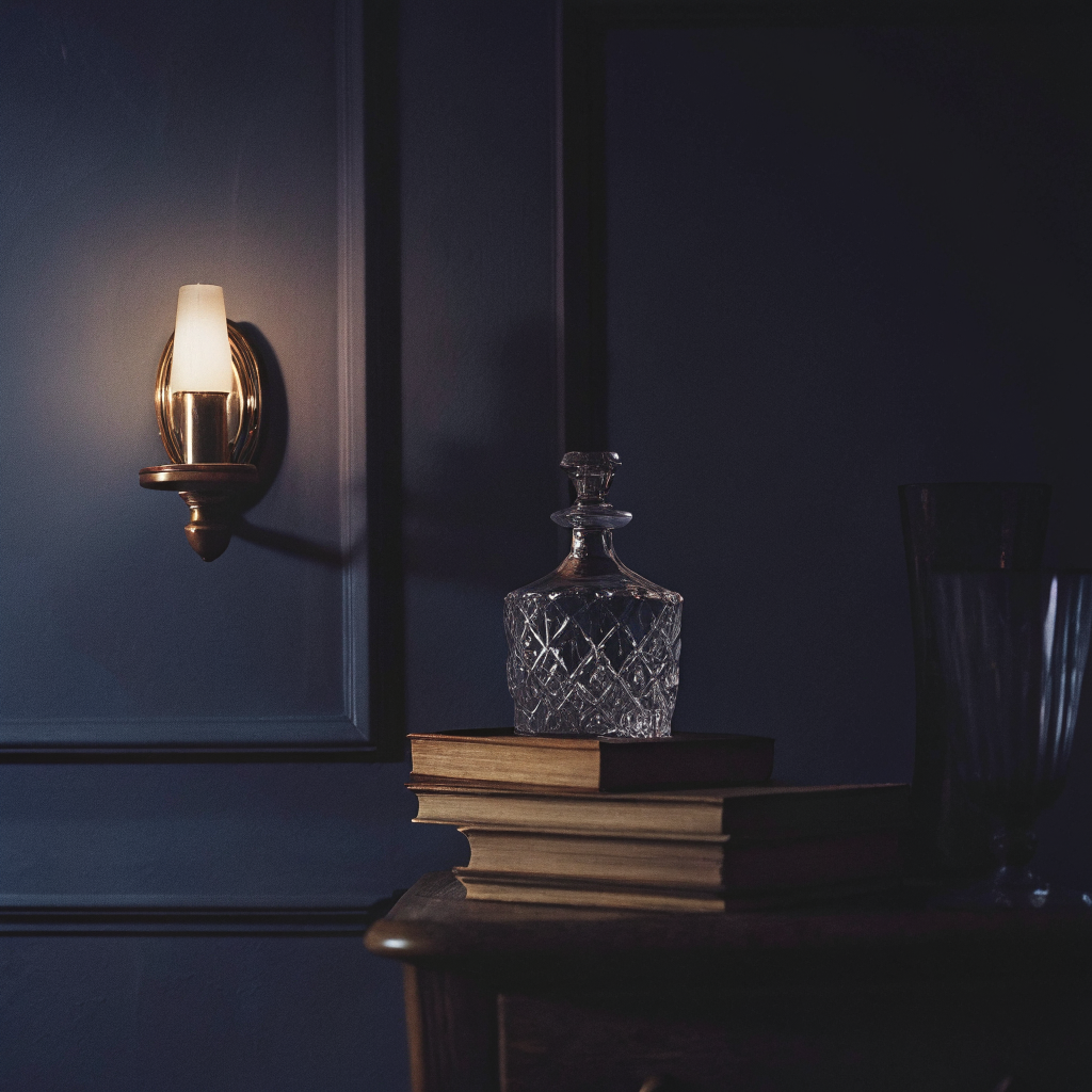 Aged brass wall light and cut-glass decanter against aubergine panelling