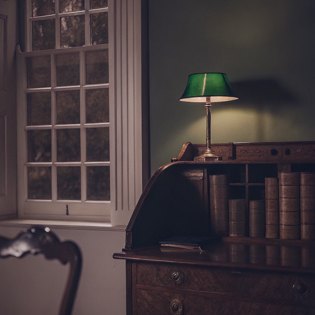 Writing desk with green glass lamp against deep green walls